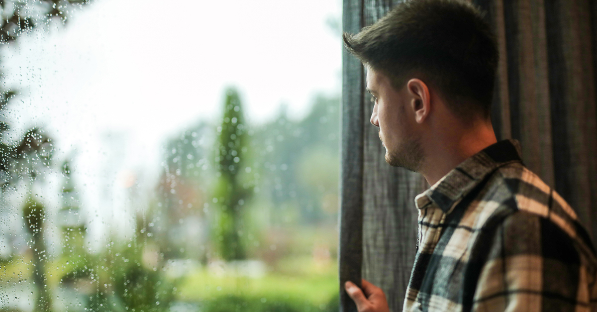 A young man looks out the window on a rainy day